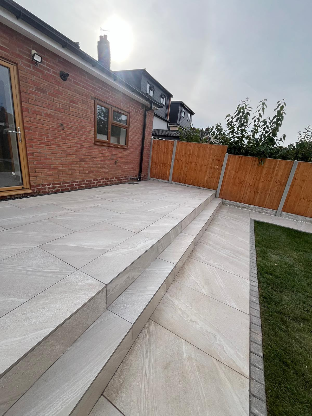 Grey porcelain slab patio with stepped level and lawn edge