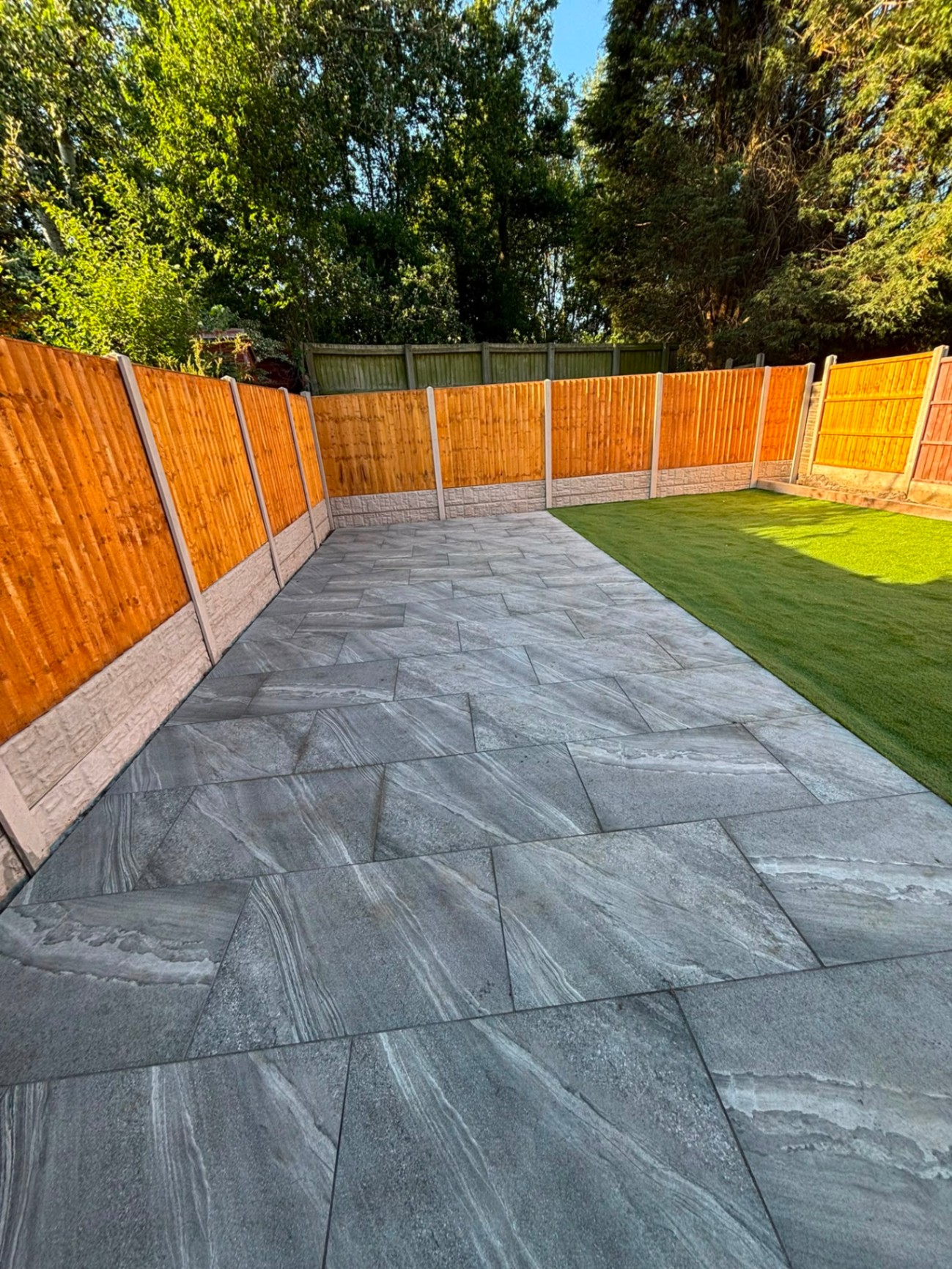 Grey stone-effect porcelain patio running to a lawn with new close-board fencing